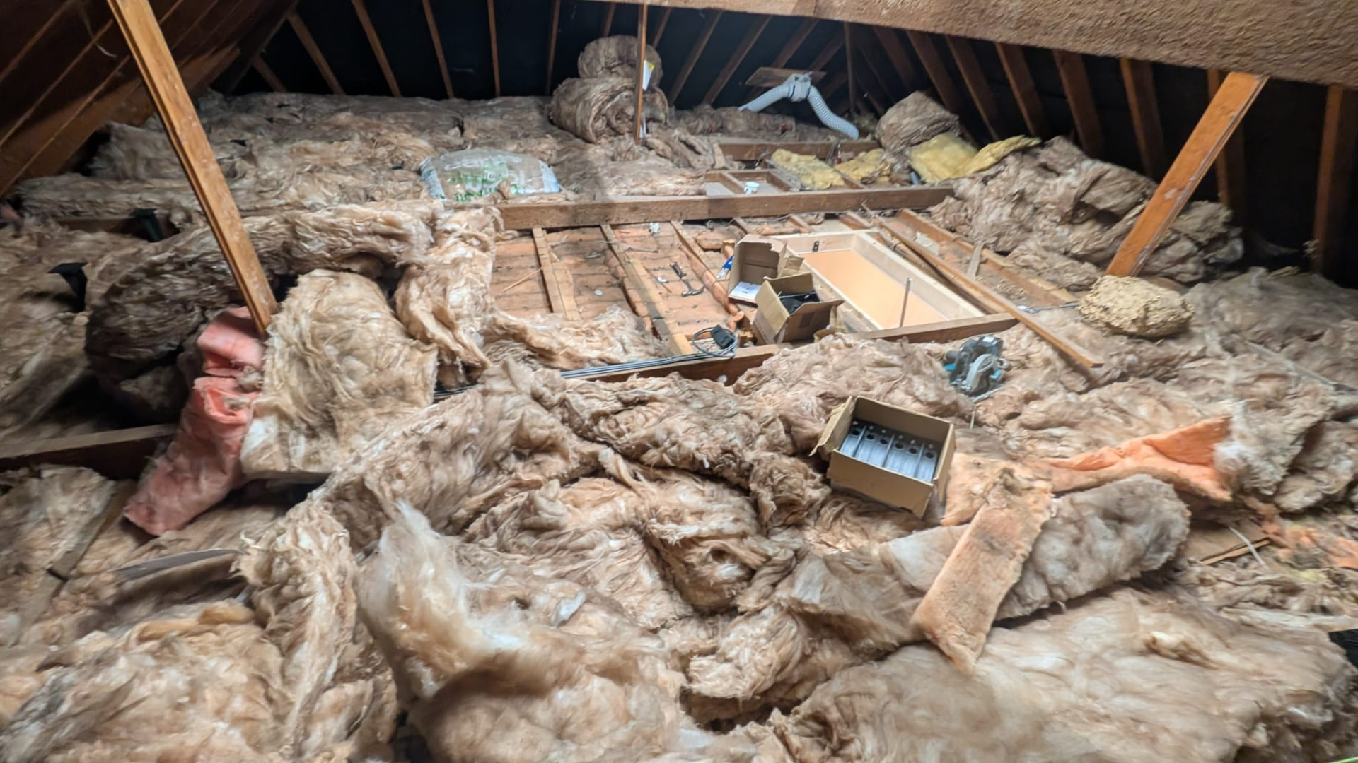 Loft before install, old insulation rolled back, tools and offcuts across bare joists