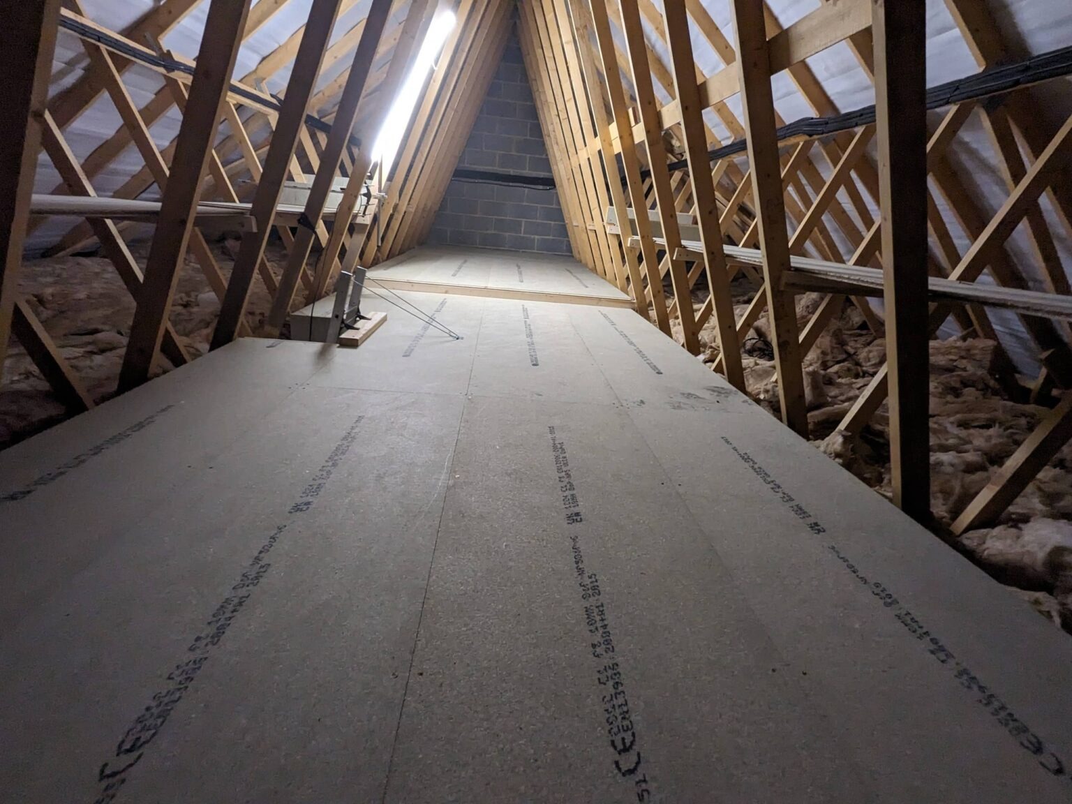 Boarded loft walkway lit by fluorescent strip lighting